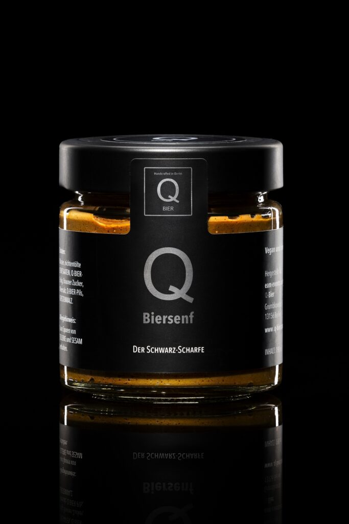 Ein Glasbehälter mit schwarzem Deckel und Q-Logo vor schwarzem Hintergrund.