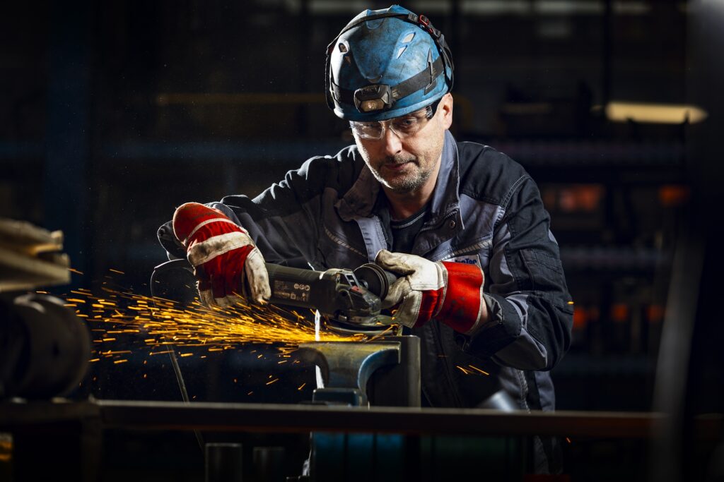 Ein Mitarbeiter mit dunklem Schutzhelm und Arbeitshandschuhen blickt auf ein Werkstück.