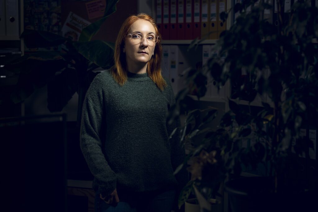 Eine Mitarbeiterin mit schulterlangen Haaren und grünem Oberteil vor einem dunklen Hintergrund.