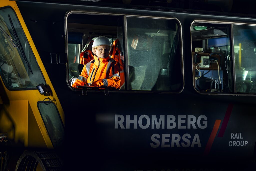 Ein Mitarbeiter in orangefarbener Warnkleidung sitzt im Führerstand eines Fahrzeugs.