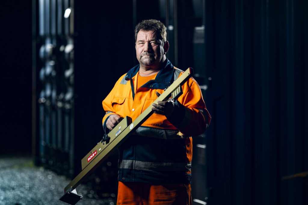 Ein Mitarbeiter in orangefarbener Arbeitskleidung hält ein Werkzeug vor sich.