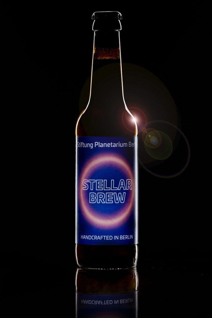 Eine Bierflasche mit blauem Etikett vor schwarzem Hintergrund mit einem Lichtreflex.
