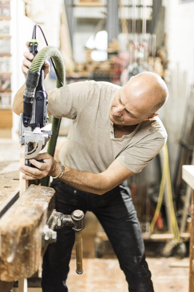 Ein Tischler beugt sich über ein Werkstück und setzt ein elektrisches Bohrwerkzeug an.