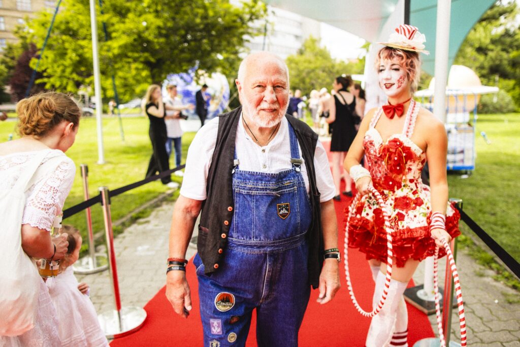 Ein lächelnder Besucher steht neben einer auffällig rot kostümierten Person.
