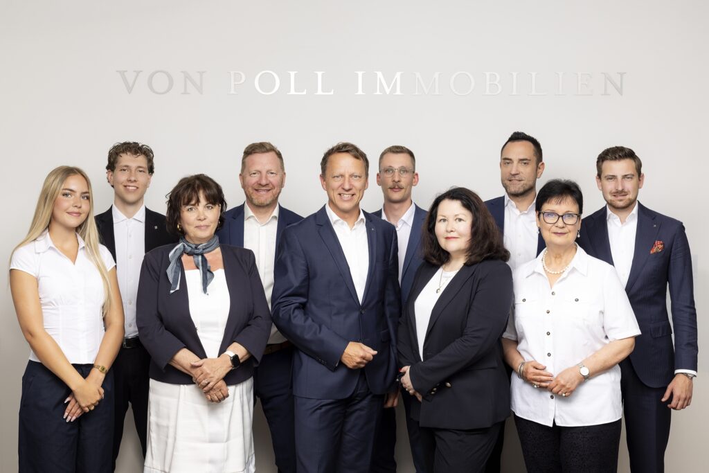 Das Team von VON POLL IMMOBILIEN steht gemeinsam vor einer hellen Wand mit Firmenschriftzug.
